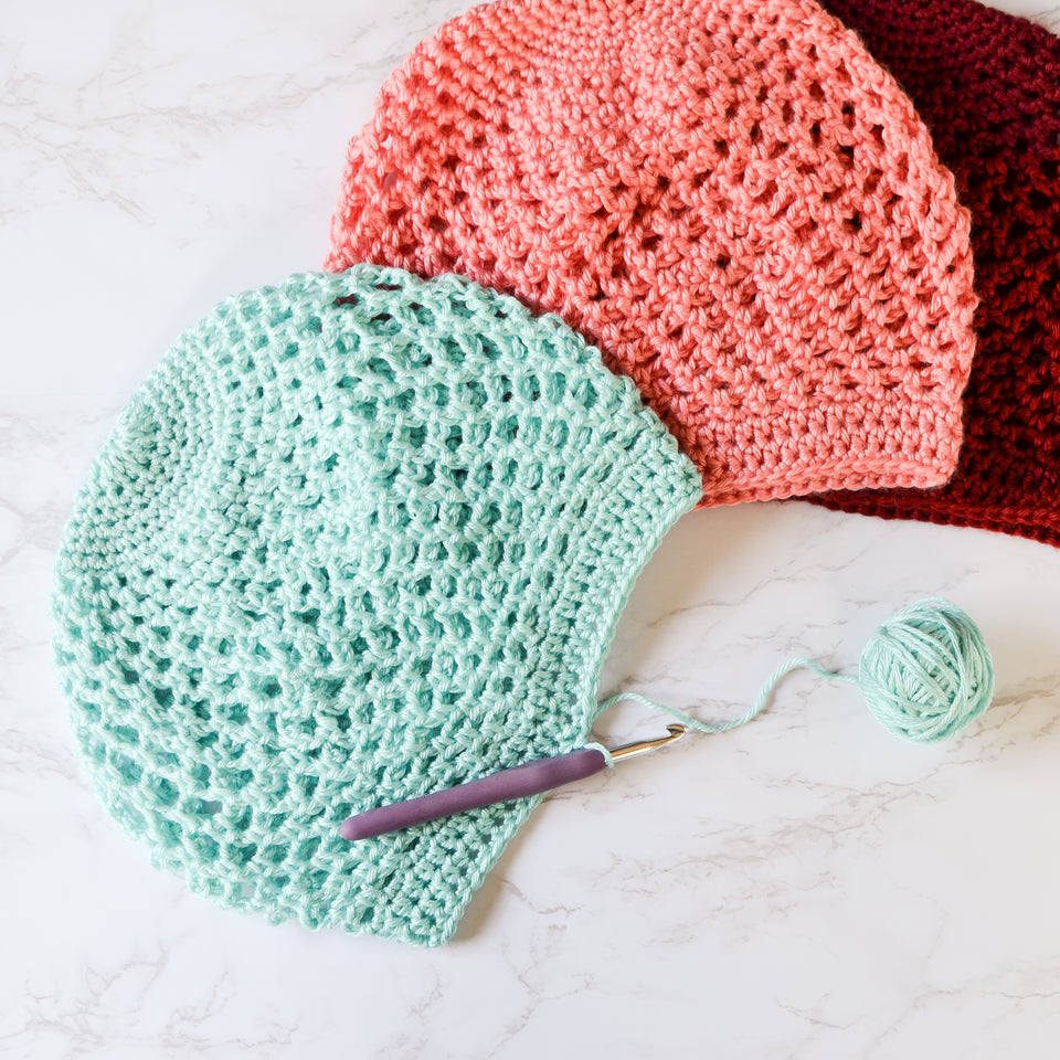 A stack of crochet Adventure Beanies in turquoise, coral and burgundy.