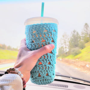 Hand holding out a turquoise coffee sleeve on a large tumbler cup