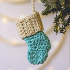 Blue and cream crochet Christmas stocking ornament hanging from a tree.