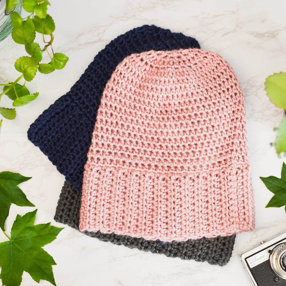 A stack of handmade beanie hats in pink, gray and navy blue.